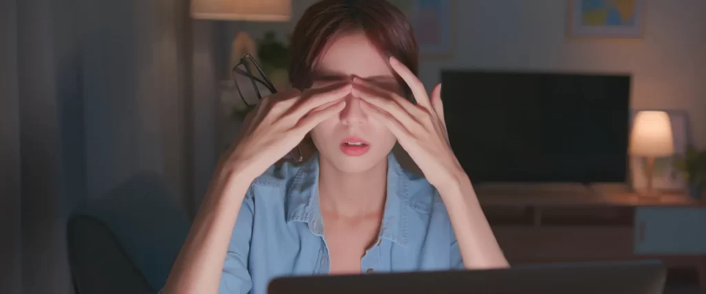 Girl rubbing her eyes while in front of the laptop